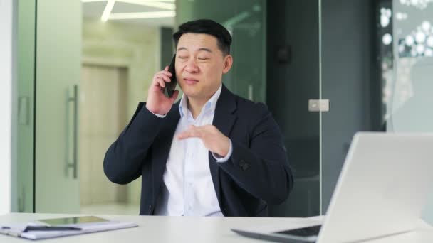 Uśmiechnięty Azjatycki Biznesmen Rozmawiający Smartfonie Siedząc Nowoczesnym Biurze Szczęśliwy Pozytywny — Wideo stockowe