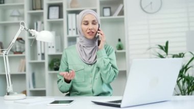 Müslüman satış temsilcisi telefon danışmanı bir müşteriyle konuşuyor. Gülümseyen Arap İslami kadın çalışan ofis çalışanı, girişimci ve danışman akıllı telefonlar konuşan kapalı alan iletişimi