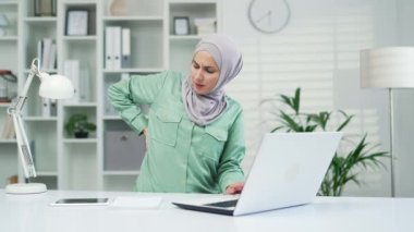 Modern işyeri girişimcisi ofis çalışanlarının bilgisayarlarında çok çalıştıktan sonra sırtı ağrıyan aşırı yorgun Müslüman bir iş kadını, kapalı alandaki gerginlikten muzdarip.