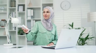 Woman employee entrepreneur. office worker Turn on a remote control air conditioner, cooling system or humidifier. business Female Sitting at work at a computer desk. Workplace, changing temperature