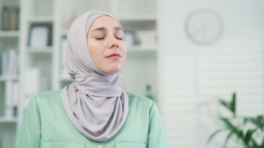 Portre kapanıyor, genç, çekici, mutlu Müslüman kadın ofiste soğuk havadan hoşlanıyor, gözlerini kapatıyor, tesettürlü işçi kadın derin bir nefes alıyor, rahatlıyor ve evde dinleniyor.