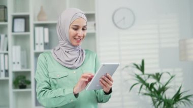 Genç müslüman kadın ofis çalışanı ofiste dikilirken dijital tablet kullanıyor. Profesyonel iş kadını, iş kadını, tarama cihazı kapalı alanda. 