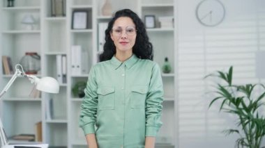 Ofiste ya da ofis odasında kameraya bakıp gülümseyen çekici İspanyol kadının portresi. Mutlu Arap Latin kadın girişimci ya da serbest çalışan. 