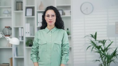 Ofis işyerinde ya da ofis odasında kameraya bakan kendine güvenen genç bir kadının portresi. Ciddi bağımsız Arap, Latin kökenli, serbest çalışan ve kollarını kavuşturmuş bir girişimci.