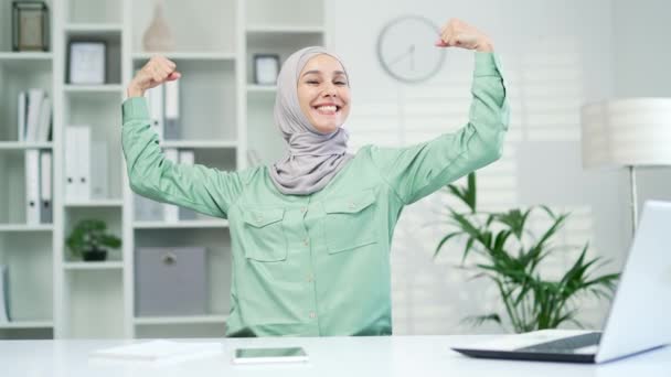 カメラを見て強い自信を持つイスラム教徒の女性従業員ビジネスマンの肖像画や強さのジェスチャーを示しています オフィスの職場でヒジャーブの幸せな女性は 筋肉を二足歩行を示しています屋内 — ストック動画