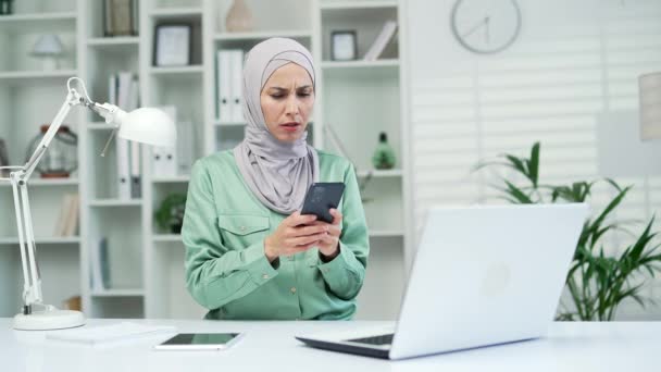 若いイスラム教徒の女性オフィス労働者の従業員は 負の結果の通知を受信し 職場で携帯電話のスマートフォンを保持悪いニュースを読む ヒジャーブ州のフリーランスの起業家で動揺した女性 — ストック動画