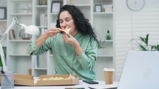 若い女性労働者が職場のパソコンでピザを食べています オフィスでのフードデリバリー 幸せな従業員ランチカメラでのランチタイムの様子 — ストック動画