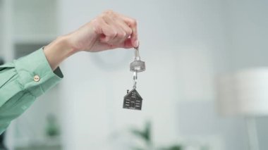 Kadın eli evin ya da dairenin anahtarlarını evin arka planında tutuyor. Gayrimenkul satın alma, ofis kiralama, finansal konut kredisi veya tasarruf ve sigorta kapatma kavramı