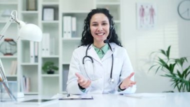 Webcam görüntüsü. Kablosuz kulaklıkla gülümseyen kadın doktor hastane kliniğinde video konuşmasında konuşuyor. Mutlu doktor, ofiste otururken kameraya bakan hastaya danışıyor.