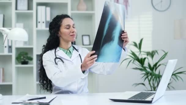 有信心的女医生穿着白色外套 坐在医院诊所的办公室里检查X光照片 布鲁内特医生正在仔细研究一张肺的照片 — 图库视频影像