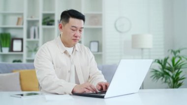 İç işlerinde masa başında otururken dizüstü bilgisayarda yazan özgüvenli Asyalı adam. Freelancer bir projede uzaktan bilgisayar üzerinde çalışıyor, çevrimiçi bir sohbette bir müşteriyle iletişim kuruyor.