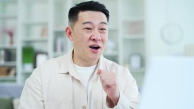 Kapatın. Asyalı kendine güvenen iş adamı merkez ofiste otururken bilgisayarla konuşuyor. Gülümseyen bir koç veya öğretmen çevrimiçi bir eğitim, seminer, eğitim, kurs veya webinar yürütür.