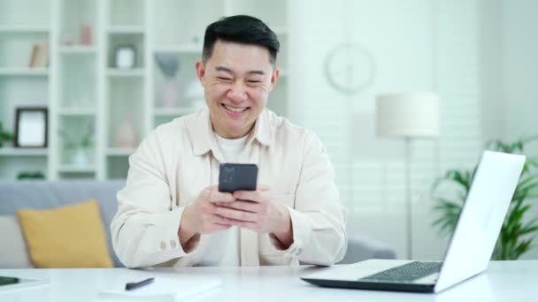 Feliz Asiático Homem Usando Smartphone Enquanto Sentado Mesa Local Trabalho — Vídeo de Stock
