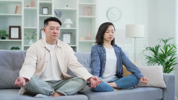 一对亚洲夫妇坐在客厅的沙发上 双目紧闭地沉思着 在舒适的沙发上 穿着休闲装的夫妻安静下来 安安静静地躺在舒适的沙发上 — 图库视频影像