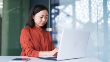 Modern ofisteki iş yerinde masa başında otururken bilgisayarında daktilo kullanan Asyalı bir iş kadını. Bilgisayarda bir proje üzerinde çalışan kendine güvenen bir bayan çalışanın internet üzerinden bir müşteriyle mesajlaşması.