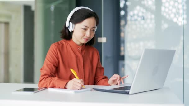 Ασιάτισσα Γυναίκα Ασύρματα Ακουστικά Που Σπουδάζει Καθισμένη Στο Γραφείο Βλέποντας — Αρχείο Βίντεο
