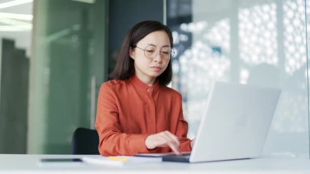 在现代办公室工作时 过度劳累的亚洲女商人在笔记本电脑上工作时眼睛感到紧张 疲惫的女员工摘下眼镜和按摩 擦鼻梁 — 图库视频影像