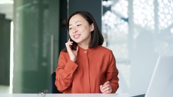 Щаслива Дружня Азіатка Розмовляє Смартфону Сидячи Робочим Столом Сучасному Офісі — стокове відео