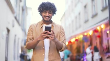 Genç, yetişkin iş adamı gülümseyen şehir caddesinde cep telefonu online harita uygulaması geziyor ve şehir manzarasının tadını çıkarıyor. Akıllı telefonlu mutlu yakışıklı turist dışarı çıkıyor.