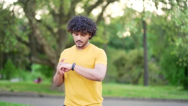 在城市公园 年轻的赛跑选手在聪明的手表上查看训练结果 他们感到很失望 穿着T恤衫的瘦弱英俊男子对戴在漂亮手镯上的指示器不满意 — 图库视频影像