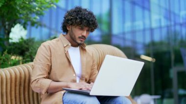 Bir ofis binasının yanındaki bankta otururken dizüstü bilgisayardan harika haberler okuyarak başarıyı kutlayan mutlu adam. Gülümseyen erkek neşeli bir mesaj aldı, el hareketini zaferle gösterdi, evet