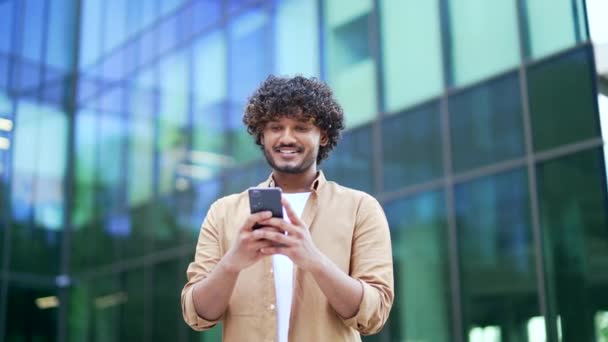 Νεαρός Χαμογελαστός Επιχειρηματίας Χρησιμοποιεί Ένα Smartphone Ενώ Στέκεται Στο Δρόμο — Αρχείο Βίντεο