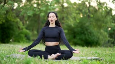 Genç sporcu kadın, şehir parkındaki bir paspasın üzerinde çıplak ayakla meditasyon yapıyor. Spor giyimli esmer kadın dışarıda yoga yapıyor. Formda bir kadın işten sonra ya da hafta sonu gözleri kapalı dinlenir.