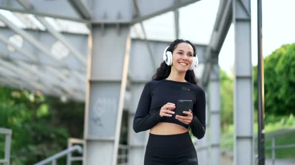 Jovem Sorrindo Mulher Andando Com Fones Ouvido Telefone Celular Gostando — Vídeo de Stock