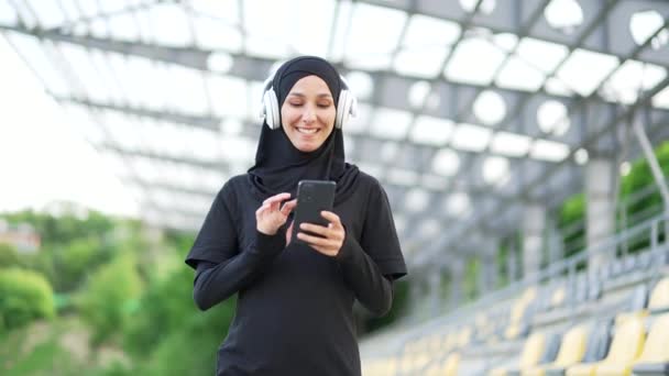 Mulher Muçulmana Desportiva Hijab Andando Com Fones Ouvido Telefone Celular — Vídeo de Stock