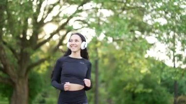 Şehir parkında koşan kulaklıklı genç bir bayan koşucu. Eşofmanlı mutlu esmer sporcu kadın müzik dinlerken dışarıda koşmaktan hoşlanıyor. Konsept spor ve sağlıklı yaşam tarzı