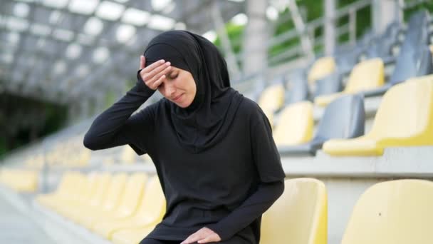 ヒジャーブ州の若いスポーティなイスラム教徒の女性は 都会のスタジアムに座っている間 頭痛を感じます 片頭痛性髄膜炎を患っている悲しい女性 高血圧 彼女は気分がよくない 医療の概念 — ストック動画