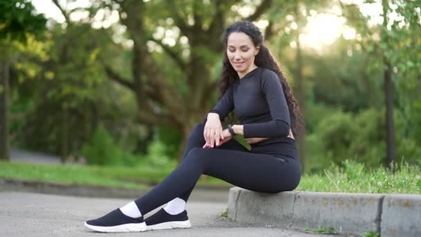 Χαμογελώντας Νεαρή Αθλήτρια Αναζητούν Έξυπνο Ρολόι Κάθεται Στο Αστικό Πάρκο — Αρχείο Βίντεο