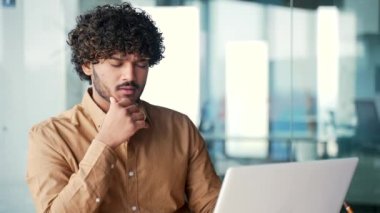 Kapatın. Modern bir ofisteki bir iş yerinde dizüstü bilgisayarın başında otururken düşünceli bir çalışan bir soruna çözüm düşünüyor. Ciddi geliştirici proje üzerinde çalışırken bilgiyi analiz eder