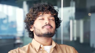 Modern bir ofiste gözleri kapalı rahatlayan genç ve yakışıklı bir çalışan. Sakin, mutlu ve derin nefes alan bir erkeğin portresi. Pozitif işçi işe ara verdi. Meditasyon kavramı