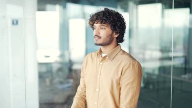 Modern ofiste kollarını kavuşturmuş başarılı yakışıklı bir adamın portresi. Tişörtlü, kıvırcık saçlı ve kameraya dostça bakan kendine güvenen bir girişimci. Kafasından vur.