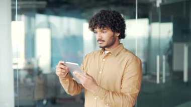 Genç bir çalışan ofiste dururken bir tablet kullanıyor. Gülümseyen bir işadamı internette sohbet ediyor, daktilo ediyor, mesaj okuyor, sosyal ağlara bakıyor veya internetten bilgi izliyor