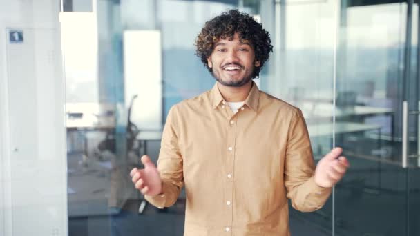 一个面带微笑的年轻人站在一间现代化的办公室里看着摄像机时的肖像 积极友善的商人拍手 表达积极的情感和称赞他人的表现 — 图库视频影像