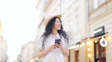 Çekici, şapkalı, genç İspanyol bir turist akıllı cep telefonuyla sokakta yürüyor internette geziniyor, teknolojiyi ve hayat tarzı seyahat ve seyahat kavramını araştırıyor.