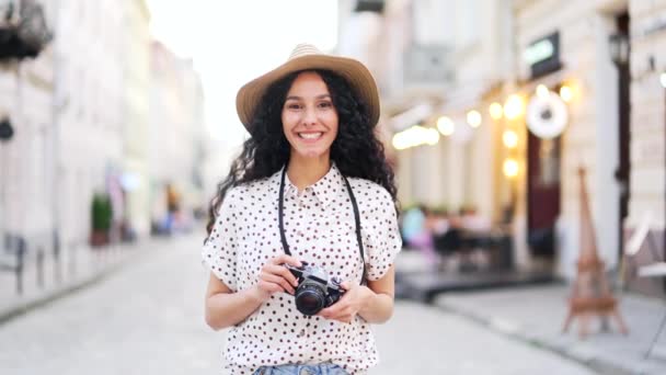 都市の町の背景に街の通りに立って帽子の肖像画の美しい幸せな若い観光客の女性 楽しいかなり旅行者巻きブルネット笑顔とカメラを見て 夏以外の屋外 — ストック動画