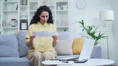Hayal kırıklığına uğramış bir kadın evdeki kanepede oturan büyük faturalara bakıyor. Maaş çeki tutan, ev bütçesi ve finansal harcamaları düşünen üzgün bir kadın.