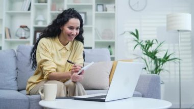 Bayan öğrenci evdeki kanepede otururken uzaktan eğitim veren bir öğretmeni internetten dinliyor. Uzaktan öğrenme seminerinde bir kadın dizüstü bilgisayarla özel öğretmenle iletişim kurar.