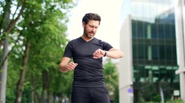 Şehir sokaklarının arka planında akıllı görünümlü bir sporcu. Akıllı bilezik kullanan bir koşucu. Portre kondisyoncusu sonuçları kontrol ediyor. Erkek sporcu giyimi koşusu sonuçtan memnun