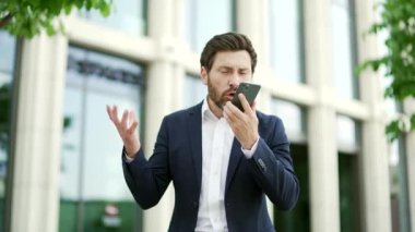 Kızgın işadamı dışarıda dururken elinde akıllı telefon tutarak duygusal konuşuyor. Shirty sinirli yetişkin patron girişimci resmi takım elbiseli bir ofis binasının önünde telefonda tartışıyor.