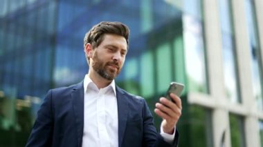 Cep telefonu kullanan yakışıklı sakallı bir iş adamı. Yetişkin bir adam mesaj atıyor. Ofis Bölgesi 'nde dururken akıllı telefonuyla sohbet ediyor. İş için. Sosyal Ağ Teknolojisi İnsanları. Uygulama