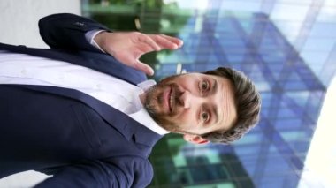POV dikey çekim, başarılı iş adamının video görüşmesi ofis binasının dışında takım elbiseli bir iş adamı akıllı telefon kamerasına bakıp gülümsüyor ve iş arkadaşlarıyla çevrimiçi konuşurken eğleniyor.