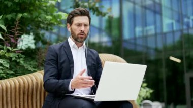 Hüzünlü işadamı, modern ofis iş merkezinin yanındaki bankta oturan dizüstü bilgisayarında kötü haber ya da olumsuz sonuç içeren e-postalar okuyor. Açık hava caddesi.