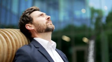 Depresyondaki iş adamı resmi takım elbiseli girişimci ofis binasının yanındaki bankta oturuyor. Yakın mesafede depresyonda olan üzgün erkek yatırımcı zihinsel sağlık sorunları yaşıyor.