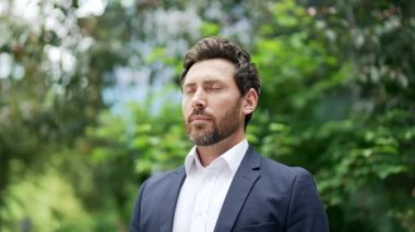 Mutlu yakışıklı işadamı rahatlar, derin bir nefes alır park meydanındaki ağaçların arasında dikilirken ya da ormanda resmi takım elbiseli iş adamı dışarıda kapalı gözlerle eğlenirken.