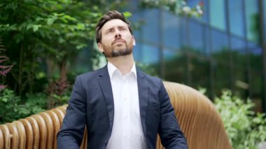 Çalışanlar, modern bir ofis binasının yanındaki bankta otururken boyun ağrısından muzdaripler. İş adamı rahatsız ve sırt ağrısı hisseder. Yorgun ve yorgun bir adam oturarak çalışmanın ardından acı hisseder.