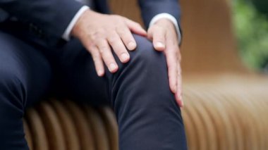 İş adamı diz veya eklem ağrısından muzdarip. Yakından yetişkin bir erkek, dışarıda bankta otururken ağrıyan bacağına masaj yapar. Kasılmadan sonra dizine masaj yaparken ellerini kapat.